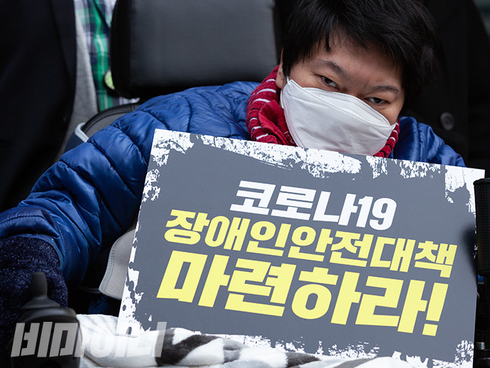 장애인 활동가가 하얀 마스크를 쓰고 “코로나19 장애인 안전대책 마련하라”라고 적힌 손팻말을 들고 있다. 사진 박승원
