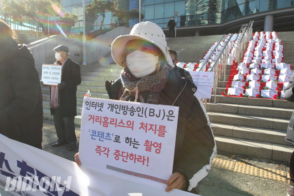 로즈마리 홈리스야학 학생회장이 피켓을 들고 서 있다. 피켓에는 '인터넷 개인방송인(BJ)은 거리홈리스의 처지를 '콘텐츠'로 하는 촬영 즉각 중단하라!'라고 적혀 있다. 사진 하민지