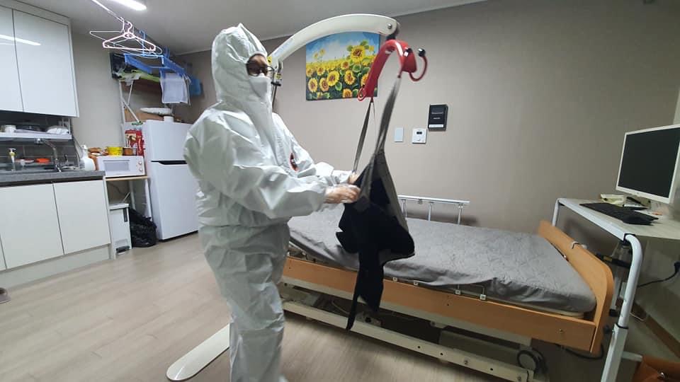 지난 16일, 확진 판정을 받은 정영만 씨의 자택에서 배우자가 방호복을 입고 정 씨를 침대로 옮기기 위해 리프트에 슬링을 걸고 있다. 정영만 씨 제공. 