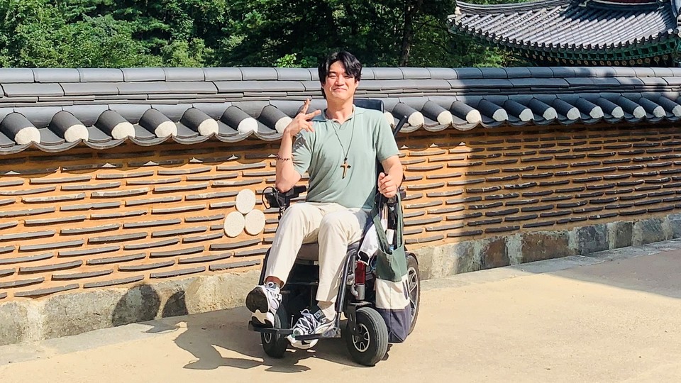유진우 씨가 휠체어에 앉아 손가락으로 '브이'를 그리고 있다. 십자가 목걸이를 착용했다. ⓒ유진우