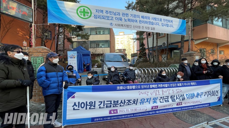 장애인권단체 활동가들이 신아원 정문 앞에서 기자회견을 열고 있다. '안전제일. 지역 주민님과 관련 기관의 배려와 사랑으로 안전하게 정리되었고 더욱 노력하여 관리하겠습니다. 감사합니다'라고 적힌 신아원 현수막 밑에 '신아원 긴급분산조치 유지 및 긴급 탈시설 이행 촉구 기자회견'이라고 적힌 장애인권단체 현수막이 펼쳐져 있다. 사진 하민지