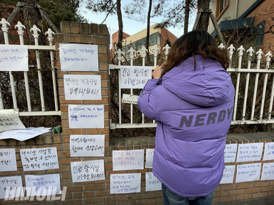활동가가 '지역사회에서 함께 살고싶습니다', '노력하면 할 수 있다! 시설 폐쇄하라'라고 적힌 피켓을 붙이고 있다. 사진 하민지