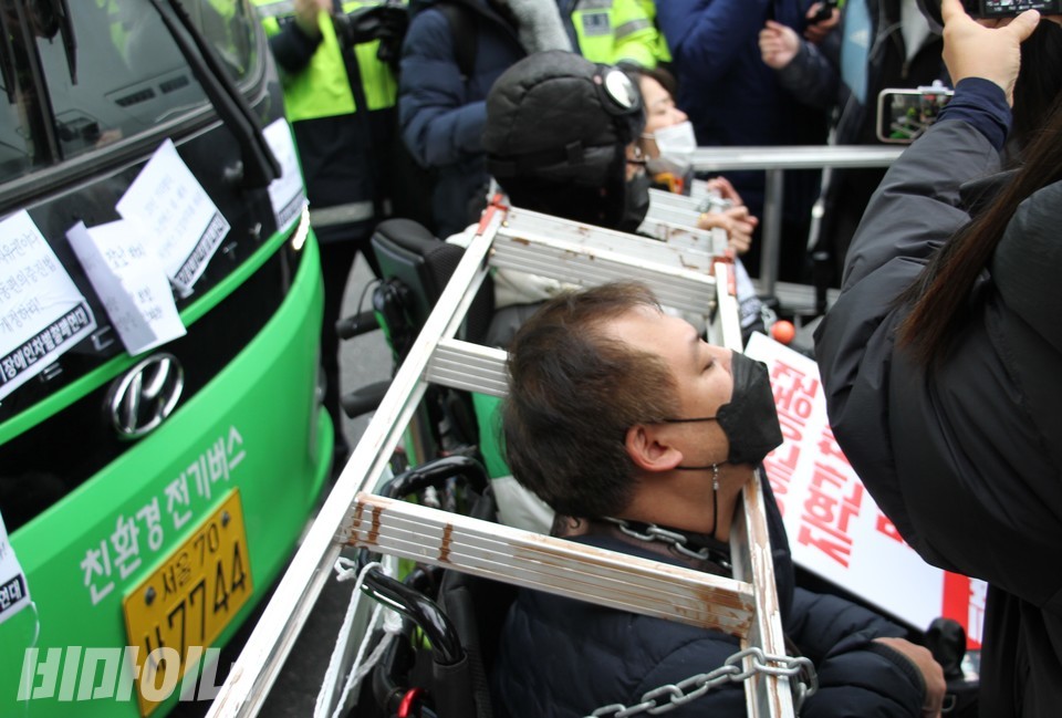 장애인 활동가들이 버스 앞에서 사다리를 목에 매고 투쟁하고 있다. 사진 이가연