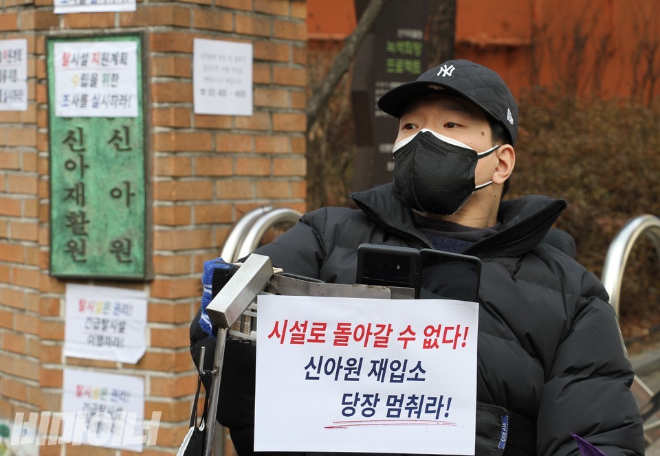 기자회견 참가자가 ‘시설로 돌아갈 수 없다! 신아원 재입소 당장 멈춰라!’라는 종이팻말을 붙이고 있다. 뒤로 보이는 신아원 현판에도 ‘탈시설 지원계획 수립을 위한 조사를 실시하라’라는 종이팻말이 붙어 있다. 사진 허현덕