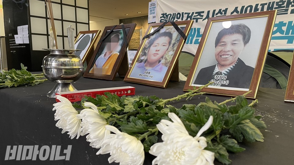 테이블 위에 국화꽃, 향, 시설희생자의 영정사진이 놓여있다. 사진 하민지