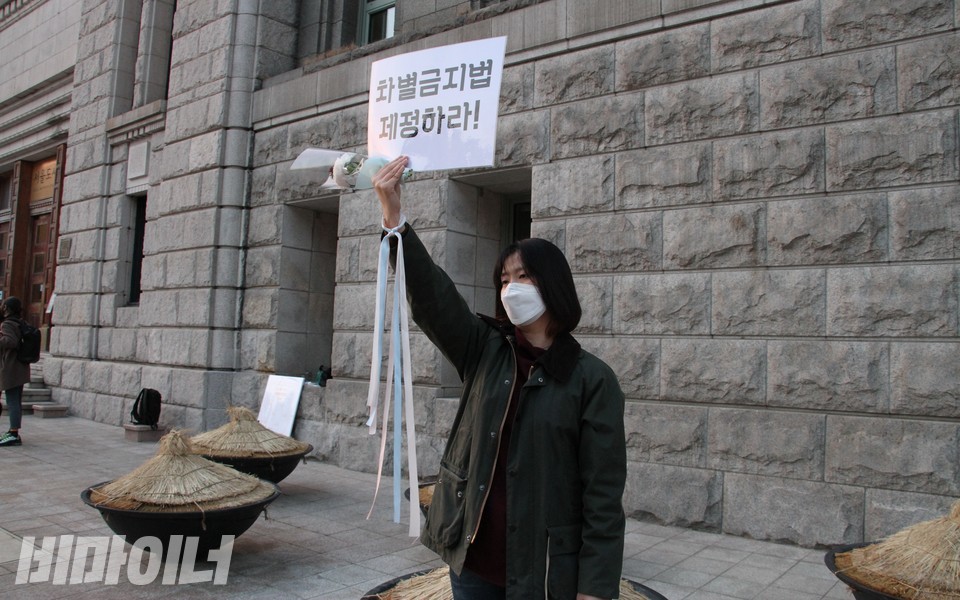 소영 씨가 '차별금지법 제정하라!'라고 적힌 피켓을 들고 1인 시위를 진행하고 있다. 소영 씨는 손목에 트랜스젠더를 상징하는 색깔의 리본을 착용했다. 사진 하민지