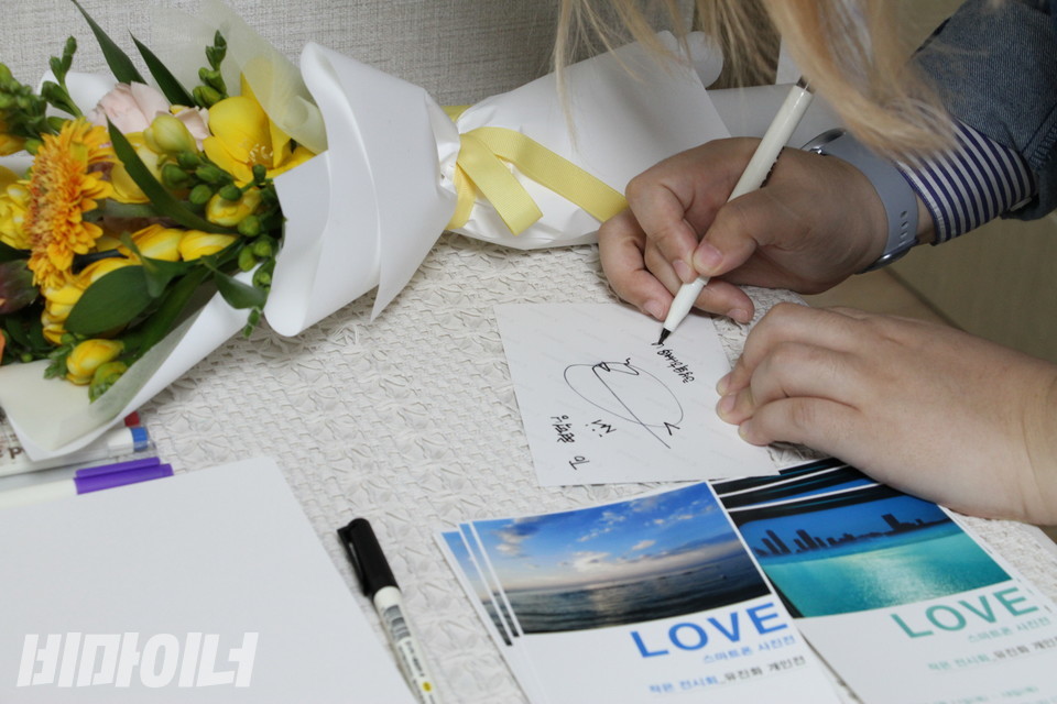 전시회에 온 사람들에게 사진이 담긴 엽서에 사인을 하고 있다. ‘TO 현덕 님, 행복하세요♡’라고 적었다. 사진 허현덕