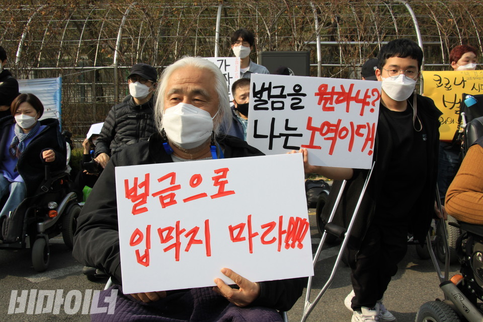 박경석 이사장(왼쪽)이 '벌금으로 입막지 마라!!!'라고 적힌 피켓을 들고 있다. 그 뒤에는 변재원 전장연 정책국장이 '벌금을 원하냐? 나는 노역이다!'라는 피켓을 들었다. 사진 하민지