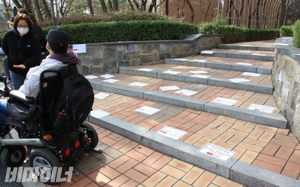 활동가들은 기자회견을 끝낸 후 계단에 장애인 이동권 보장을 촉구하는 내용의 피켓을 붙였다. 휠체어를 이용하는 김유현 두리센터 소장이 계단을 오르지 못하고 계단 앞에 머물러 있다. 사진 하민지