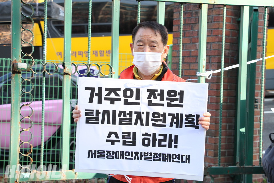 장혜영 의원이 라파엘의집에 방문한 지난 22일, 서울장애인차별철폐연대 활동가가 라파엘의집 정문 앞에서 피켓을 들고 있다. ‘거주인 전원 탈시설지원계획 수립하라! 서울장애인차별철폐연대’라고 쓰여 있다. 사진 허현덕