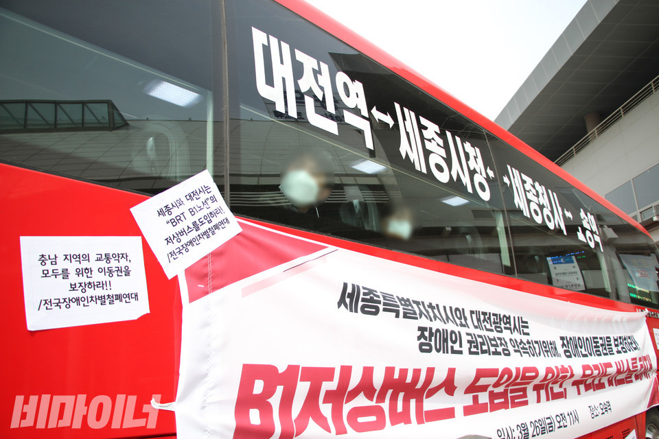 장애인은 탈 수 없는 B1버스를 장애인 활동가들이 점거하면서 버스가 출발하지 못하자 승객들이 어리둥절해하며 창밖을 둘러보고 있다. 차벽에는 B1저상버스 도입을 촉구하는 현수막과 손피켓이 붙어 있다. 사진 강혜민