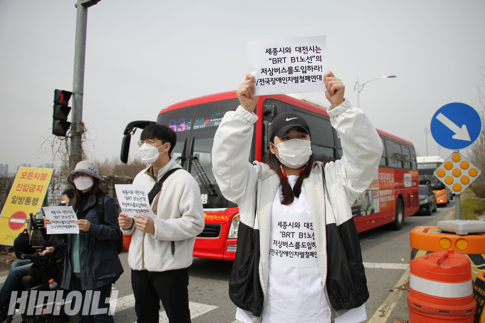 오송역 앞 버스승강장 출구를 막아선 활동가들. 손피켓에는 “세종시와 대전시는 BRT B1노선의 저상버스를 도입하라”고 쓰여 있다. 사진 강혜민