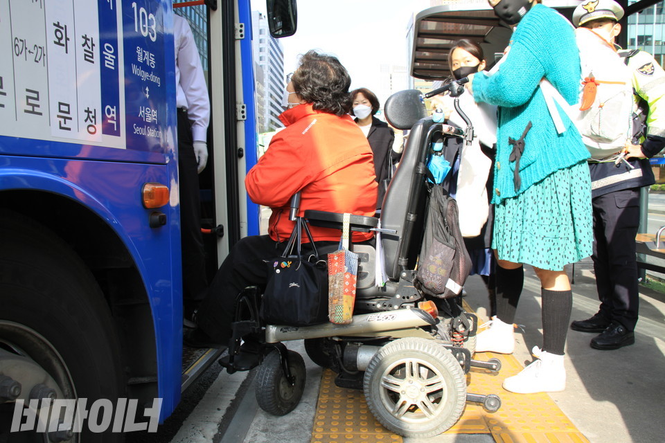 이형숙 공동대표가 '차별버스'를 멈춰 세우고 버스 기사에게 휠체어 이용자인 자신이 버스에 탈 수 있는지 묻고 있다. 일부 시민은 출근길에 이게 뭐하는 짓이냐고 이 대표를 비판하기도 했다. 이 대표 뒤로 비장애인 활동가와 시민, 경찰이 서 있다. 사진 하민지