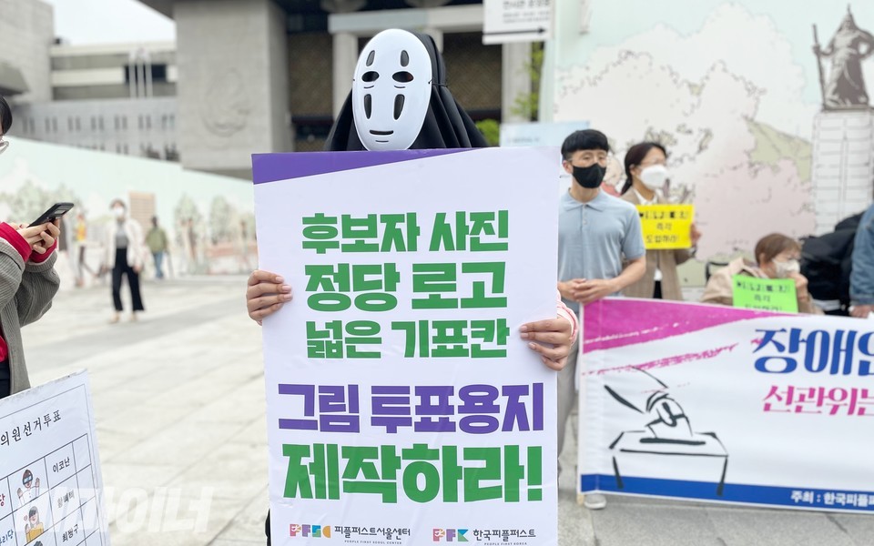 가오나시 분장을 한 활동가가 ‘후보자 사진 정당 로고 넓은 기표칸 그림 투표용지 제작하라’라고 적힌 피켓을 들고 있다. 사진 하민지