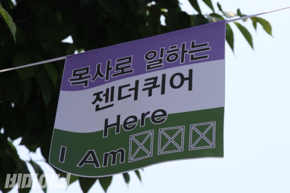 젠더퀴어 플래그에 ‘목사로 일하는 젠더퀴어, Here I Am(제가 여기 있습니다)’이라고 적혀 있다. 사진 하민지