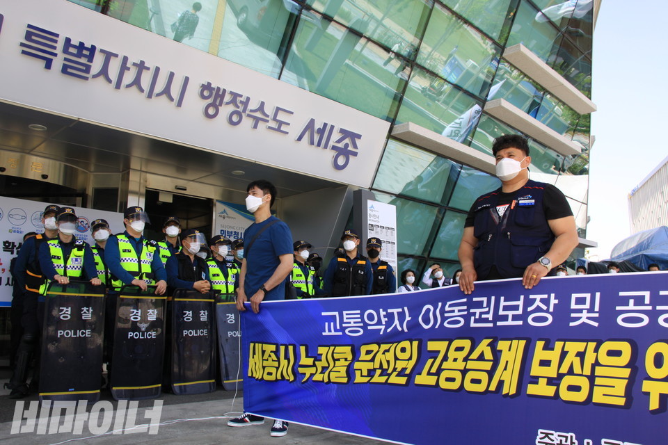 세종시청 정문 앞. ‘특별자치시 행정수도 세종’이라 적힌 간판 아래 경찰 여러 명이 방패로 무장하고 시청을 지키고 있다. 공공우수노조 조합원들이 들고 있는 현수막에는 ‘교통약자 이동권 보장’, ‘세종시 누리콜 운전원 고용승계 보장’ 등의 문구가 적혀 있다. 사진 하민지
