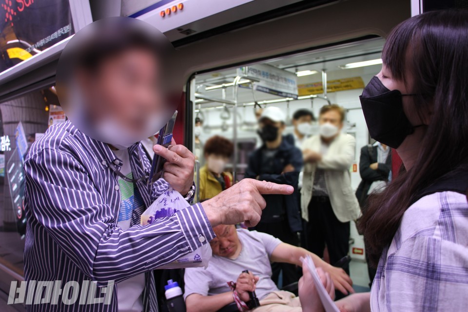 한 중년 남성이 여성활동가를 향해 삿대질하고 있고 지하철 안에는 다른 승객들이 팔짱을 끼고 지켜보고 있다. 사진 이가연