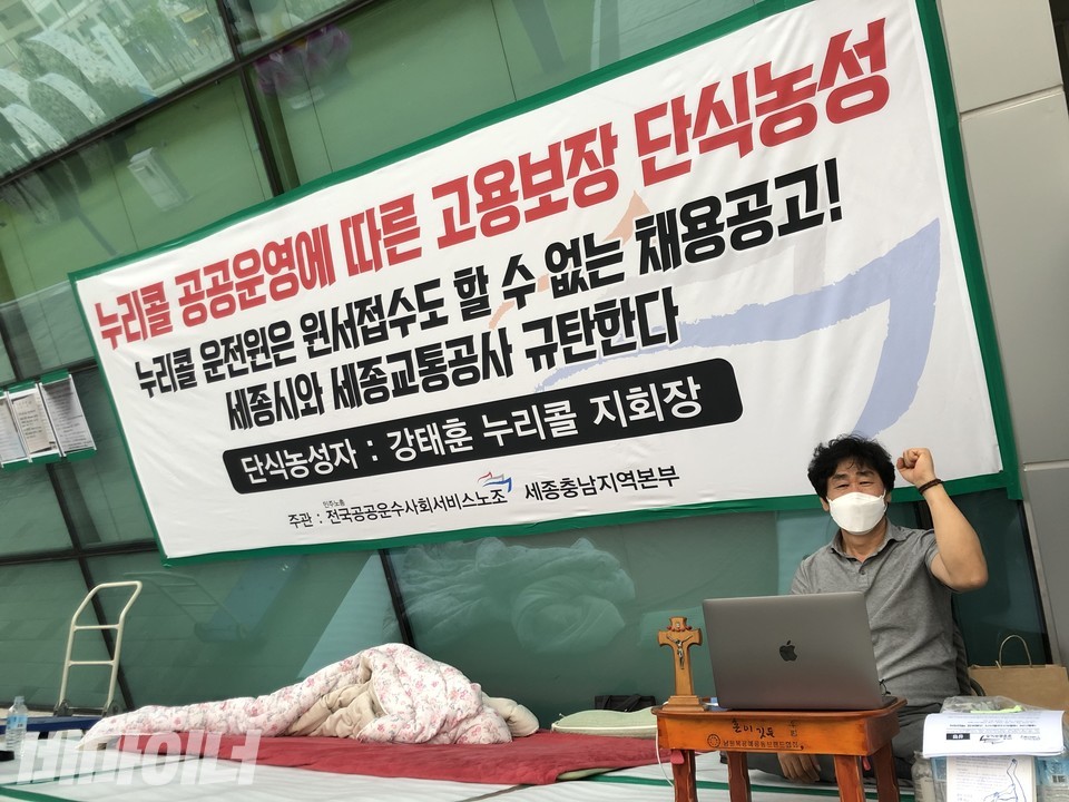 세종시청 앞에서 지난달 20일, 누리콜 공공운영에 따른 고용보장을 촉구하며 단식 농성을 하고 있는 강태훈 누리콜 지회장이 “투쟁”을 외치며 왼쪽 주먹을 들어 보이고 있다. 사진은 단식 4일째인 지난달 23일의 모습. 교자상 위에는 아내가 챙겨준 십자가가 있으며, 그의 옆에는 그가 밤에 몸을 뉘는 전기장판과 이불이 놓여 있다. 사진 강혜민