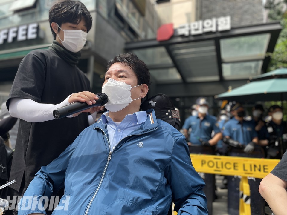최용기 한국장애인자립생활센터협의회 회장이 기자회견에서 발언하고 있다. 최 회장 뒤로 국민의힘 당사가 있고 정문 앞을 경찰 수십 명이 지키고 있다. 경찰 앞에 폴리스 라인이 처져 있다. 사진 하민지