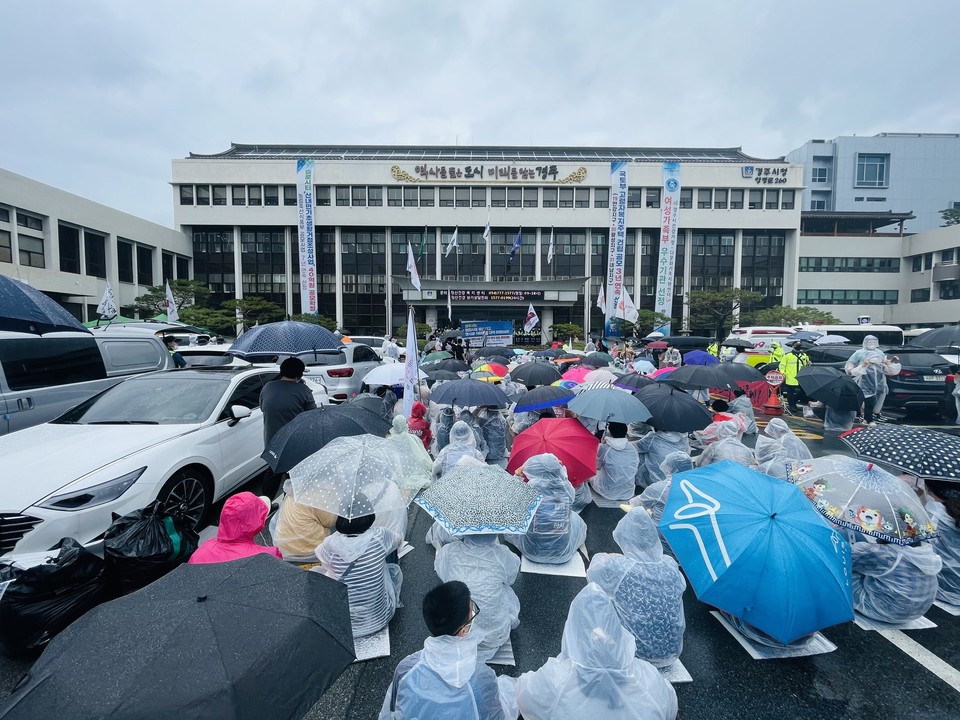 경주시청 앞 활동가들. 우산을 쓰거나 우비를 입고 바닥에 앉아 있다. 사진 경북장차연