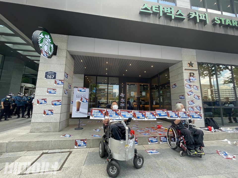 스타벅스 광화문R점 매장 앞. ‘장애인의 자유로운 이동권 보장하라’, ‘장애인 편의시설 설치 의무화하라’, ‘보건복지부는 장애인접근권 차별부다’라고 적힌 스티커 피켓 수십 장이 매장 앞에 붙어 있다. 제일 왼쪽에 경찰 수십 명이 서 있다. 앞쪽에는 이규식 서울장애인차별철폐연대 상임대표(왼쪽), 박경석 전국장애인야학협의회 이사장(오른쪽)이 피켓이 붙은 사다리를 목에 맨 채 보건복지부를 규탄하고 있다. 사진 하민지