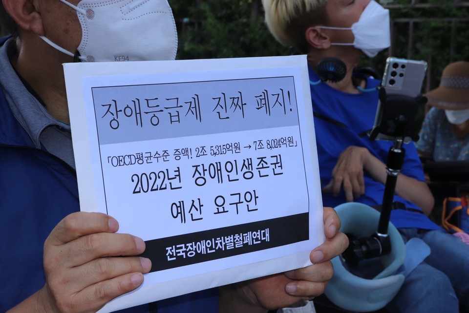 한 활동가가 ‘장애등급제 진짜 폐지! 2022년 장애인생존권 예산 요구안’을 들고 있다. 사진출처 전장연