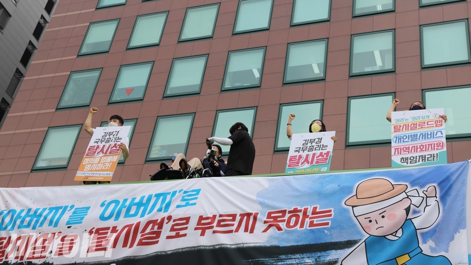 최용기 회장과 장혜영 국회의원, 그리고 장애인운동단체 활동가들이 컨테이너 옥상 위에서 주먹을 쥐고 ‘투쟁’을 외치고 있다. 사진 이가연