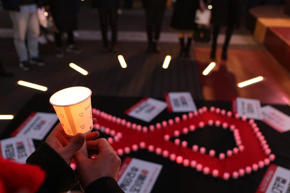 31번째 세계에이즈의 날을 맞아 2018년 11월 29일 대백 앞 광장에서 레드리본인권연대 주최로 촛불 추모제를 열었다. HIV/AIDS를 상징하는 빨간 리본이 바닥에 있고 한 사람이 촛불을 들고 있다. 사진 레드리본인권연대