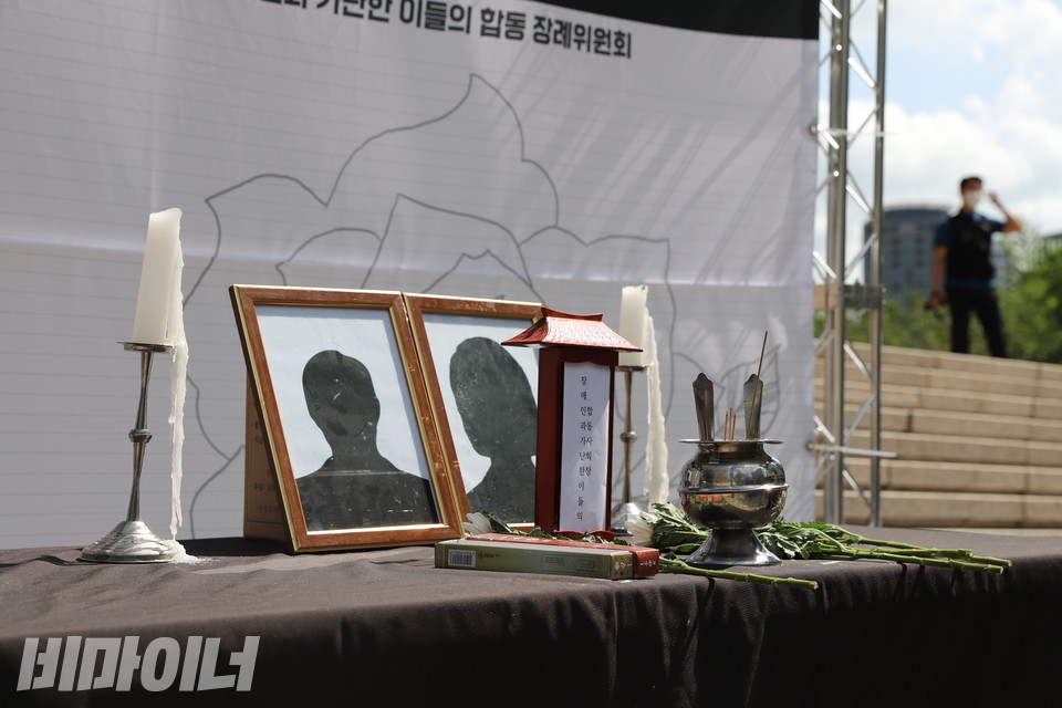 검은 천이 덮인 테이블 위에 초, 향, 국화꽃이 놓여 있다. 두 개의 영정사진 속에는 얼굴이 없다. 사진 하민지