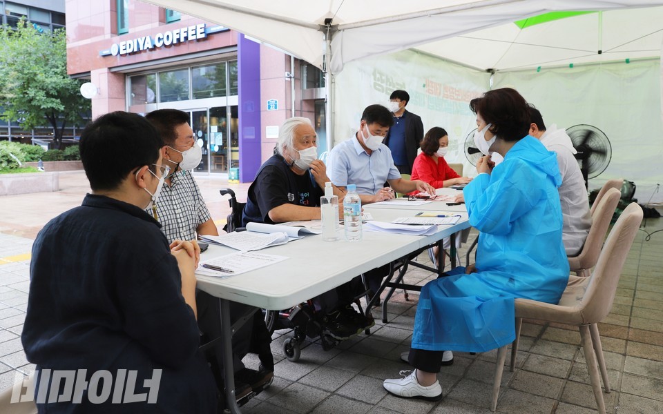 전장연과 추미애 후보와의 장애인 정책 간담회가 여의도 양대법안 농성장에서 진행됐다. 박경석 전장연 상임공동대표가 추 후보에게 장애인 정책을 설명하고 있다. 파란색 우비를 입은 사람이 추 후보. 사진 하민지