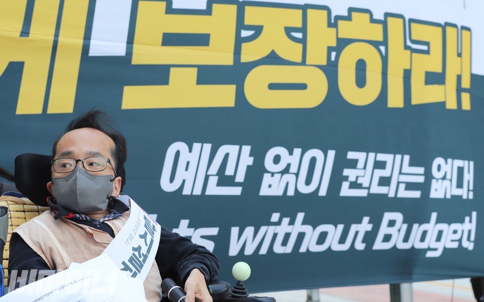 박현 한국장애인자립생활센터협의회 활동가가 ‘보장하라 예산 없이 권리는 없다’라고 적힌 현수막 앞에 있다. 사진 하민지