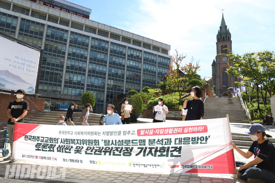 장애인인권운동단체 활동가들이 명동성당 앞에서 기자회견을 열고 있다. 현수막에는 ‘한국천주교주교회 사회복지위원회 ‘탈시설로드맵 분석과 대응방안’ 토론회 비판 및 인권위 진정 기자회견’이라고 적혀 있다. 사진 하민지