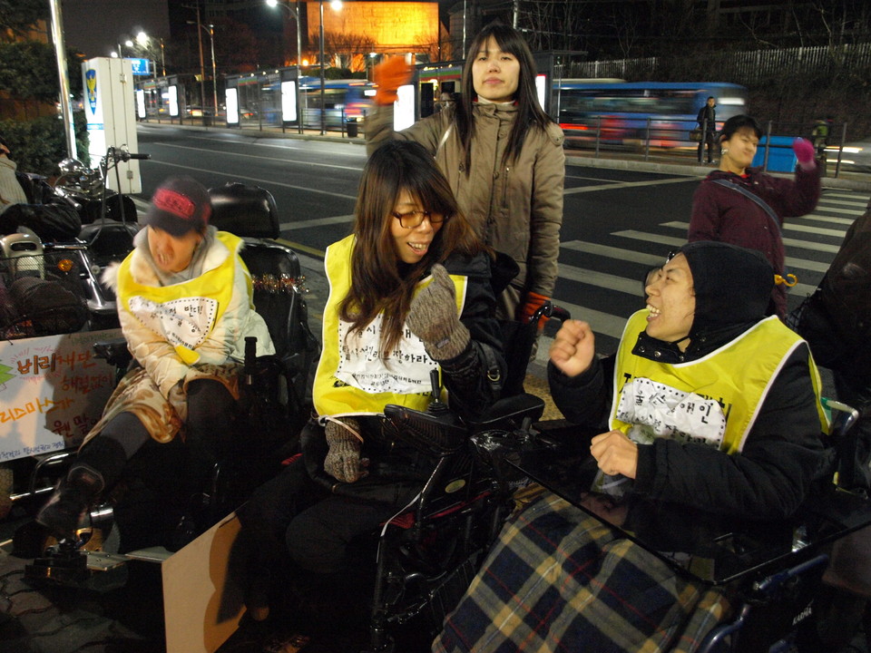 2008년 12월 24일, 탈시설 집회에 참석한 박길연 대표가 다른 장애인 활동가를 바라보며 활짝 웃으며 투쟁을 외치고 있다. 사진 김유미