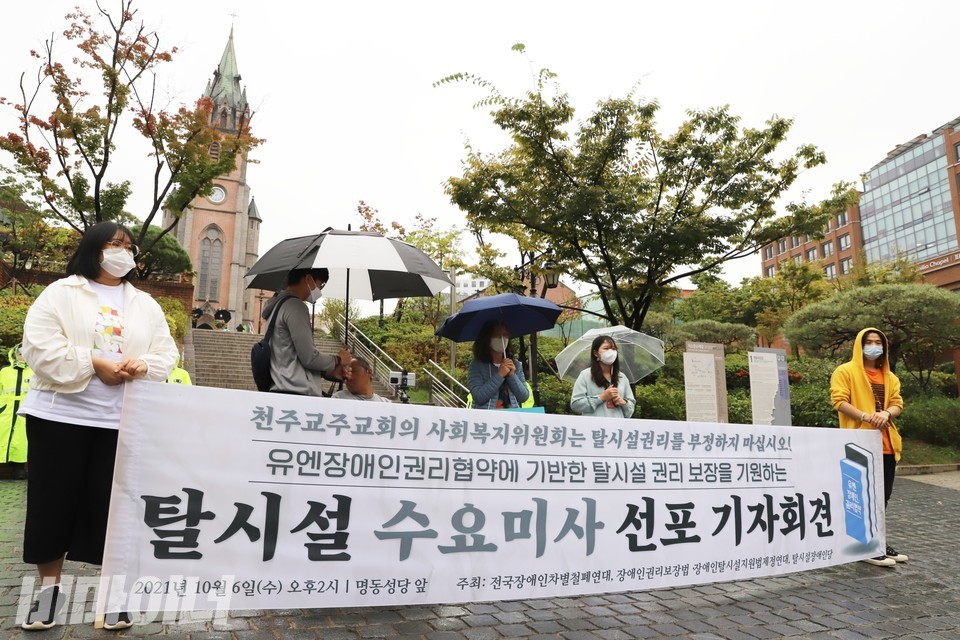 장애인운동단체 활동가들은 궂은 날씨에도 명동성당 앞에서 미사를 진행했다. 현수막에 ‘천주교주교회의 사회복지위원회는 탈시설권리를 부정하지 마십시오! 유엔장애인권리협약에 기반한 탈시설 권리 보장을 기원하는 탈시설 수요미사 선포 기자회견’이라 적혀 있다. 사진 하민지