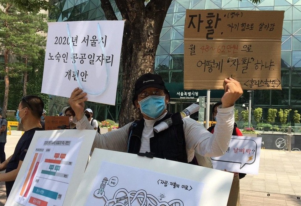한 활동가가 서울시청 앞에서 ‘자활, 명사, 자기 힘으로 살아감’, ‘월 48~62만 원으로 어떻게 자활하냐’라는 손팻말을 들고 있다. 사진 홈리스행동