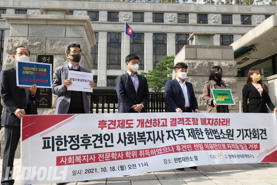 헌법소원 참여자들이 '후견제도 개선하고 결격조항 폐지하라! 피한정후견인 사회복지사 자격 제한 헌법소원 기자회견, 사회복지사 전문학사 학위 취득하였으나 후견인 선임 이유만으로 자격증 발급 거부'라고 적힌 피켓을 들고 있다. 사진 이가연