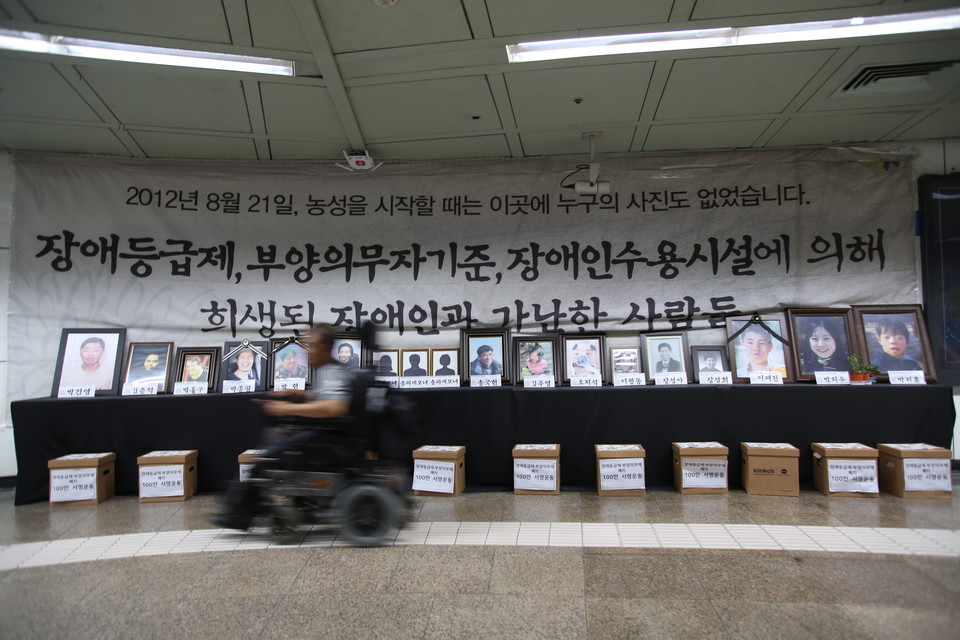 광화문 농성장에 놓인 18개의 영정. 영정 뒤 대형 현수막에는 “2012년 8월 21일, 농성을 시작할 때는 이곳에 누구의 사진도 없었습니다. 장애등급제, 부양의무자 기준, 장애인수용시설에 의해 희생된 장애인과 가난한 사람들”이라는 문구가 쓰여 있다.  사진 최인기 