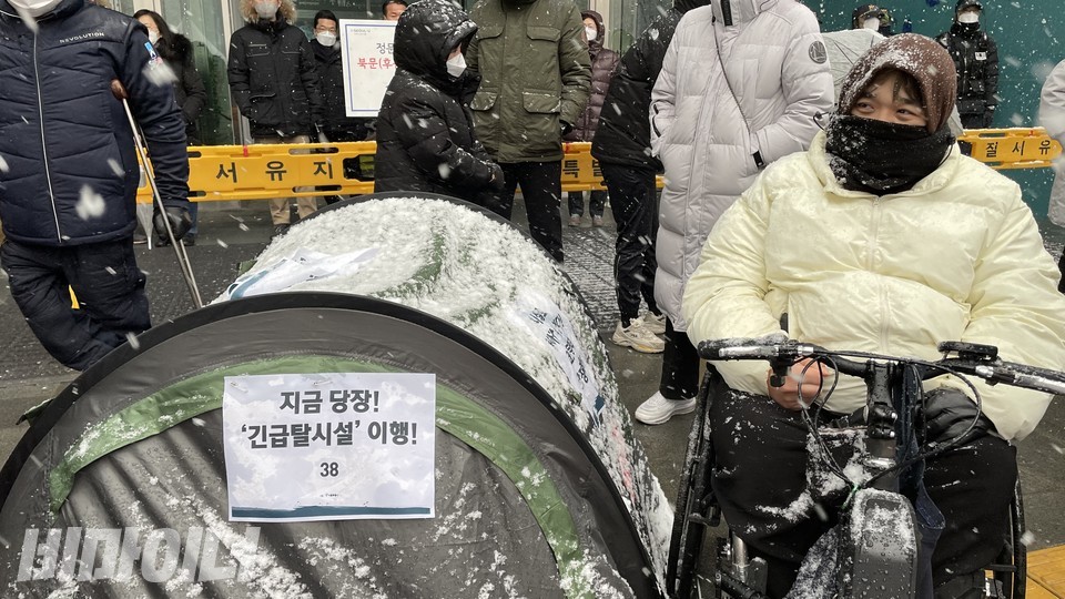 지난 1월, 서울시청 앞에서 열린 기자회견 현장. 참가자가 눈을 맞고 있다. 그의 옆에는 신아원 코로나19 확진자를 의미하는 텐트가 놓여있다. 텐트에는 '지금 당장! 긴급탈시설 이행!'이라는 피켓이 붙어있다. 사진 하민지