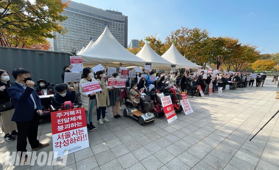 서울시청 앞 선별진료소 앞을 꽉 채운 기자회견 참가자들. ‘주거복지 전달체계 붕괴하는 서울시는 각성하라!!’ 등이 적힌 피켓을 들고 서 있다. 사진 하민지