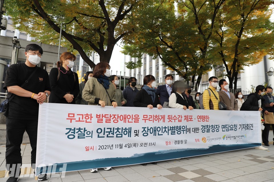 경찰청 앞 기자회견 현장. 현수막 뒤에 30여 명의 장애인운동단체 활동가들과 피해자 부모가 서 있다. 현수막에는 ‘무고한 발달장애인을 무리하게 뒷수갑 체포, 연행한 경찰의 인권침해 및 장애인 차별행위에 대한 경찰청장 면담요청 기자회견’이라 적혀 있다. 사진 하민지