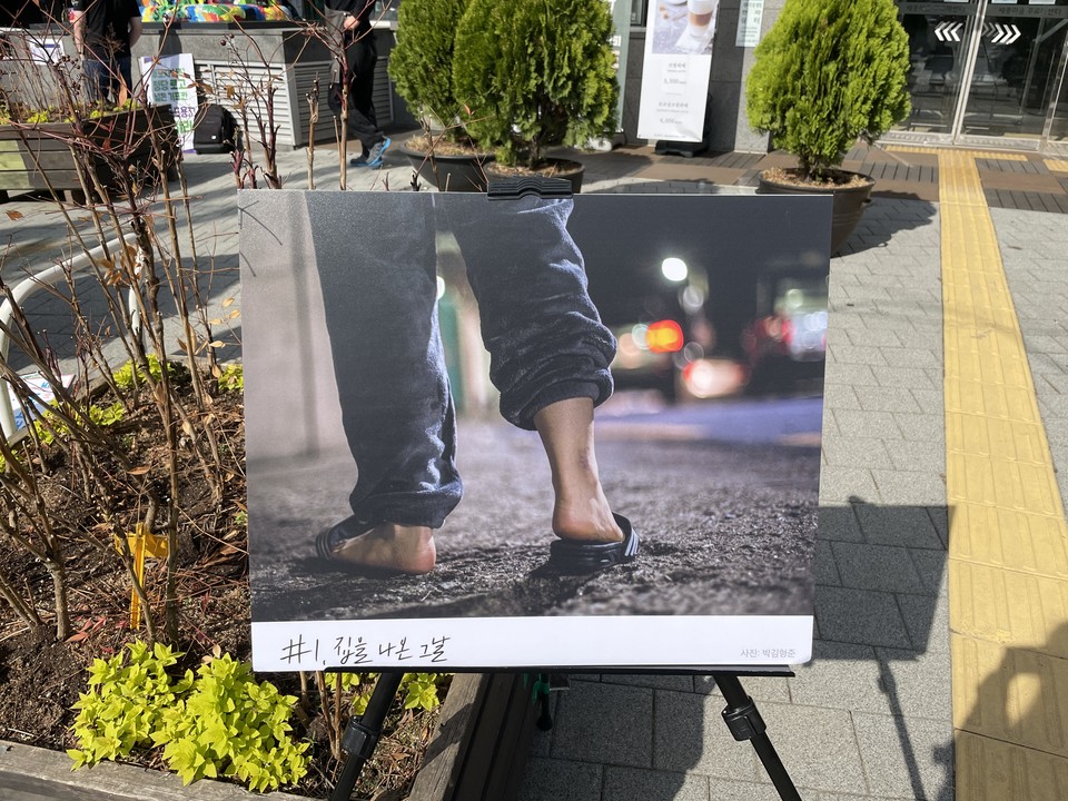 탈가정으로 인해 주거권을 보장받지 못하는 청소년은 많은 위기상황을 경험하지만, 사실 가장 먼저 경험하는 것은 막막함일 수도 있다. 츄리닝 바지를 입고 맨발로 삼선슬리퍼를 신은 채 밤거리를 걷는 다리가 담긴 사진의 제목은 ‘#1. 집을 나온 그날’이고, 사진 구석에는 ‘사진 박김형준’이라고 적혀 있다. 이 사진은 크게 인쇄되어 지지대에 세워 야외에 전시되어 있다. 청소년주거권네트워크 제공