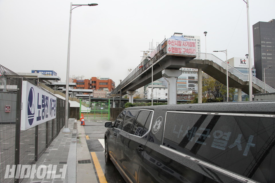 왼쪽에 ‘노량진 야구장’이라 적힌 간판이 보인다. 육교 위에는 농성장이 있다. 그곳엔 ‘수산시장 사기강탈 수협회장 구속하라’라고 적힌 현수막이 붙어 있다. 길에는 운구차가 있다. 창문에 ‘나세균 열사’라고 적힌 글씨가 보인다. 사진 하민지