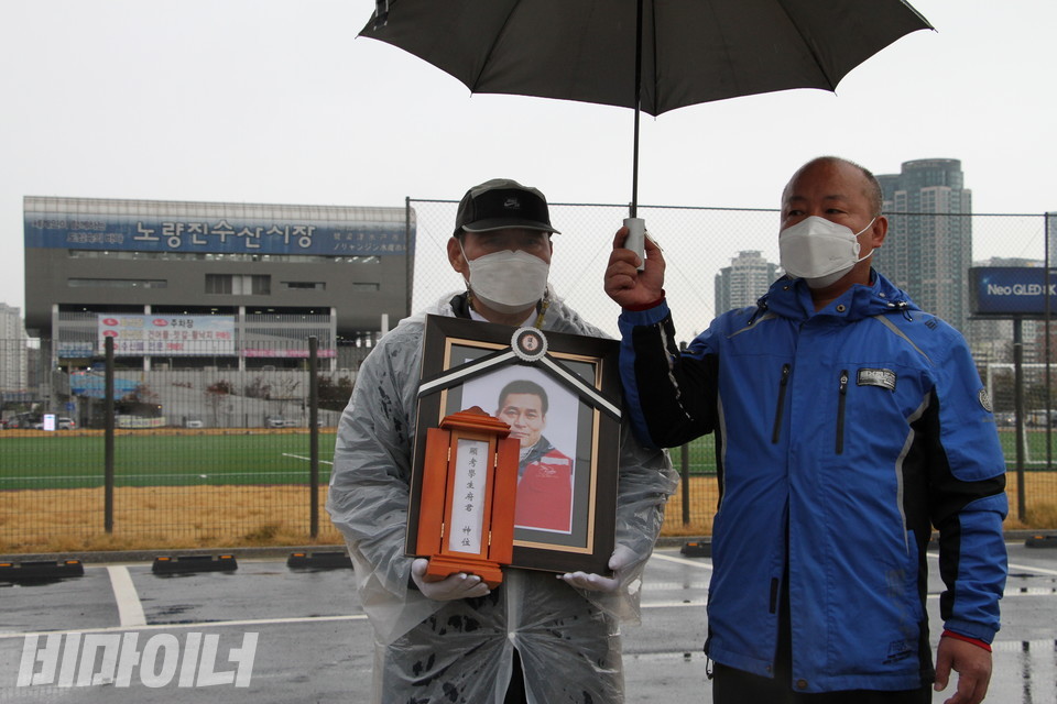 나세균 열사의 영정과 위패를 들고 있는 한상범 공동지역장. 그의 뒤로 야구장과 신 시장이 보인다. 사진 하민지