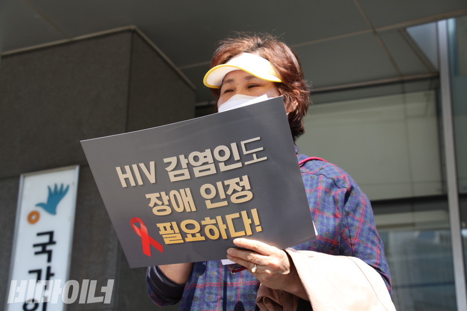지난 4월 19일, 레드리본인권연대와 장애인차별금지추진연대 등은 서울시 중구 인권위 앞에서 HIV감염인의 차별 진정 및 장애인차별금지법상 장애 인정을 촉구하는 기자회견을 열었다. 기자회견 참가자가 “HIV감염인도 장애인정 필요하다”고 적힌 손피켓을 들고 발언하고 있다. 그 뒤로 인권위 간판이 보인다. 사진 이가연