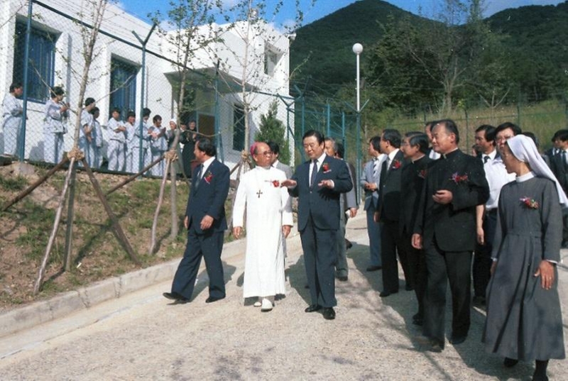 1985년 염보현 서울시장(왼쪽에서 세 번째)과 관계자들이 참석한 가운데 영보자애원 개원식이 열렸다. 철망 뒤로 하얀색 건물 앞에 같은 옷을 입은 여성 거주인들로 추정되는 사람들이 서 있다. 사진 서울사진아카이브