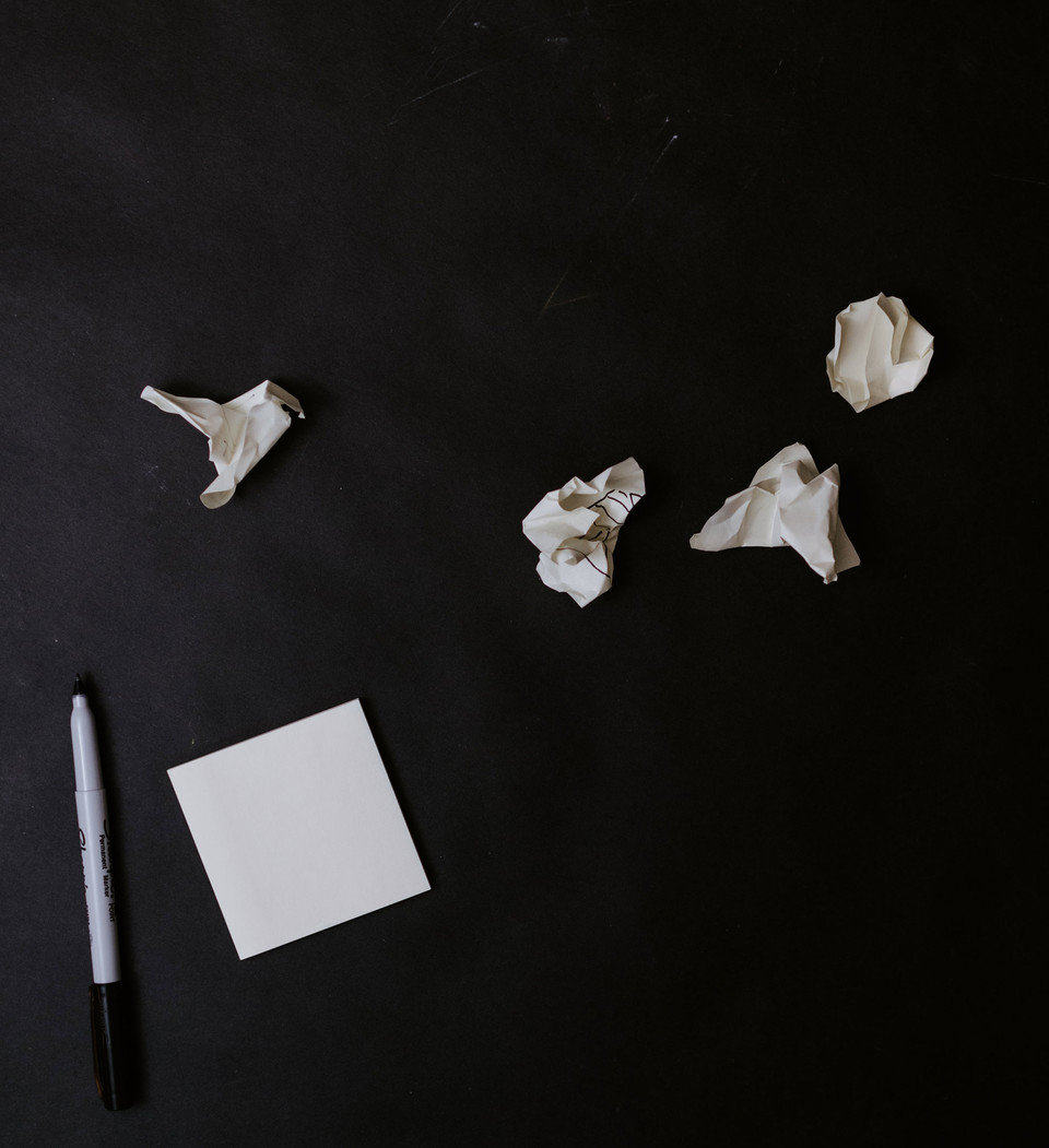 까만 사인펜과 네모난 하얀 종이가 있고, 주변에는 구겨진 종이가 여러 개 널려 있다. 사진 언스플래시 