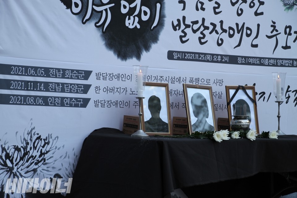 발달장애인과 그 가족의 죽음을 추모하는 단상위에 촛불과 하얀색 국화, 그리고 이름 없는 액자 사진이 놓여있다. 사진 이가연