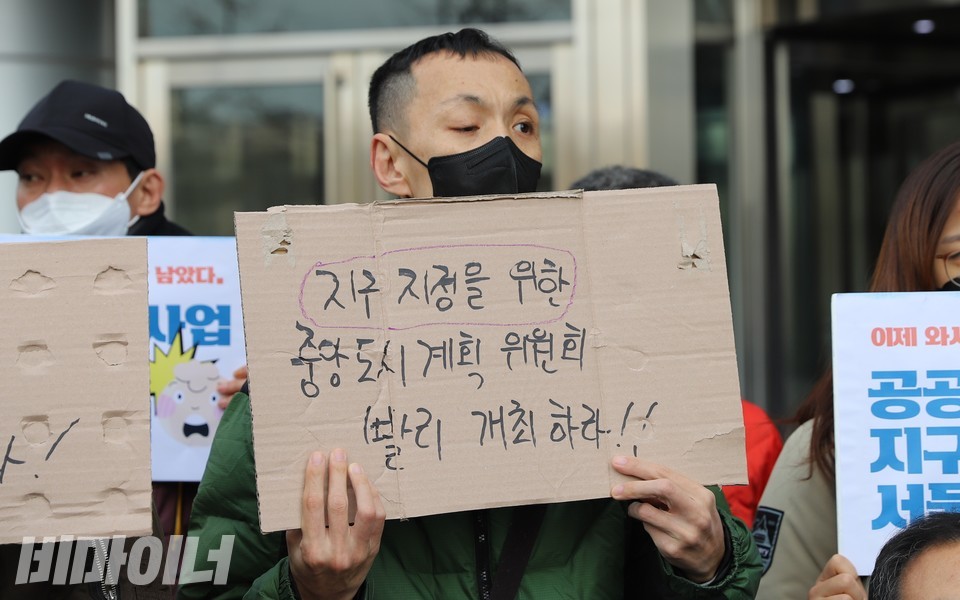 쪽방 주민이 ‘지구지정을 위한 중앙도시계획위원회 빨리 개최하라!!’라고 적힌 피켓을 들고 있다. 사진 하민지