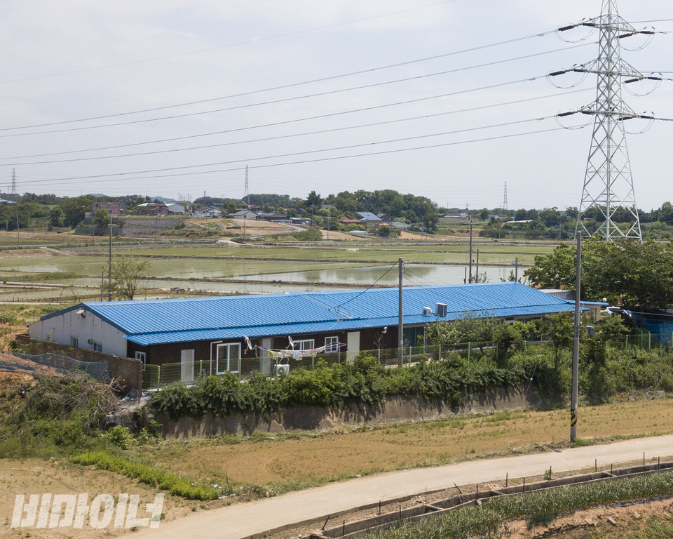 장애인 사망 사건이 발생한 미신고시설 평강타운과 개인운영시설 사랑의집이 파란색 한 지붕 아래 있는 모습. 그 옆에는 커다란 송전탑 하나가 세워져 있다. 사진 비마이너 DB