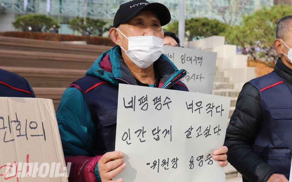 용명중 위원장이 ‘네 평 평수 너무 작다. 인간답게 살고싶다. - 위원장 용명중’이라고 적은 피켓을 들고 있다. 사진 하민지